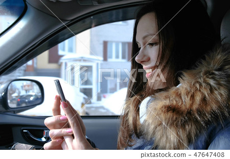 Woman in a car with a mobile phone. Young beautiful brunette woman looking something in the mobile Woman in a car with a mobile phone. Young beautiful brunette woman looking something in the mobile 47647408
