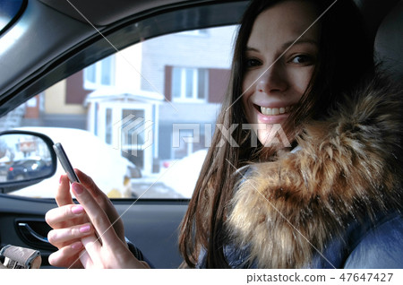Woman in a car with a mobile phone. Young beautiful brunette woman looking at camera. Woman in a car with a mobile phone. Young beautiful brunette woman looking at camera. 47647427