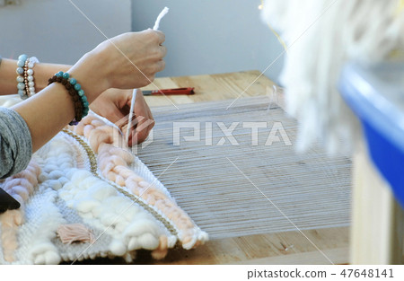 Weaving on a loom. Closeup woman's hands runs the yarn through the threads of the loom. 47648141