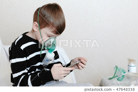 Use nebulizer and inhaler for the treatment. Boy inhaling through inhaler mask and playing the game Use nebulizer and inhaler for the treatment. Boy inhaling through inhaler mask and playing the game 47648338