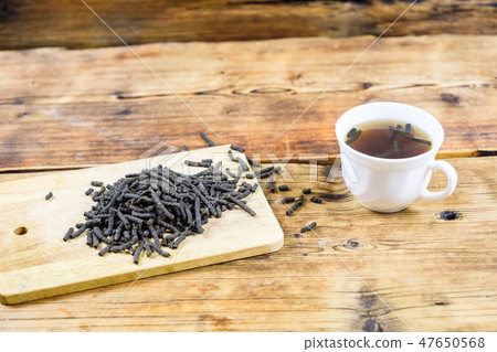 Close-up fermented Ivan-tea on wooden board. Dry herbal natural tea. White cup with Ivan-tea. 47650568