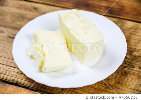 Close-up fresh farm piece of butter on a white plate on wooden background. Fresh farm products. 47650715