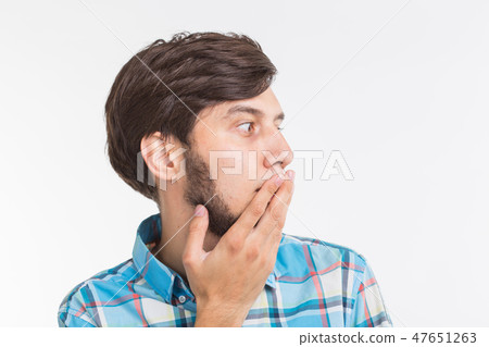 People, emotions and gesture concept - young surprised man covering his mouth with his hand on white 47651263