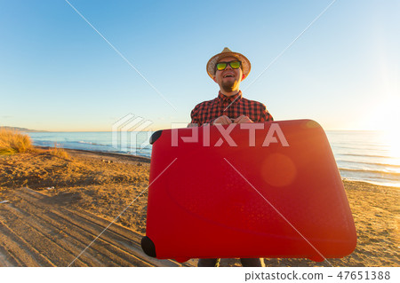 Travel and summer concept - Male tourist carrying a red suitcase at the beach Travel and summer concept - Male tourist carrying a red suitcase at the beach 47651388