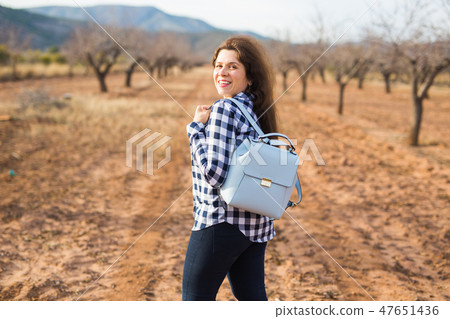 Trip, fashion and people concept - happy young woman walking with small bag and smiling over the Trip, fashion and people concept - happy young woman walking with small bag and smiling over the 47651436