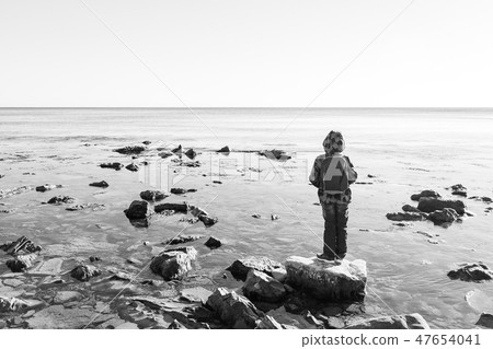 A boy stands on a rock in the black sea and looks out at the water 47654041