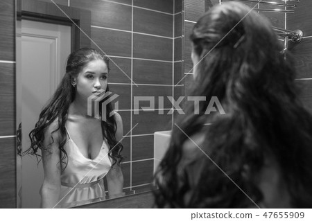 Young woman looking herself reflection in mirror at home Young woman looking herself reflection in mirror at home 47655909