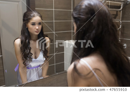 Young woman looking herself reflection in mirror at home 47655910
