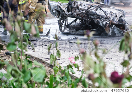 Burned car after an accident on the road. Firefighters standing nearby. Reportage picture. 47657680