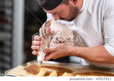 Pastry Chef with confectionary bag squeezing cream at pastry shop. 47657921