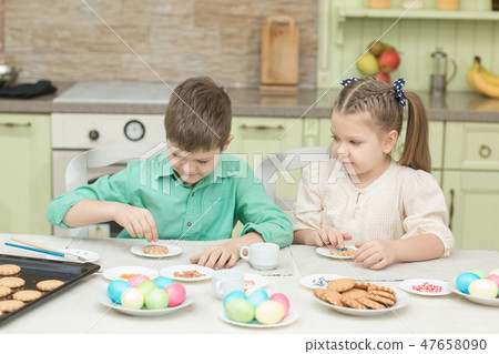 Cute children decorate cookies at a table in the home kitchen 47658090