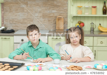 Cute children decorate cookies at a table in the home kitchen Cute children decorate cookies at a table in the home kitchen 47658092
