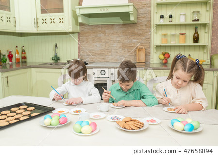 Cute children decorate cookies at a table in the home kitchen Cute children decorate cookies at a table in the home kitchen 47658094