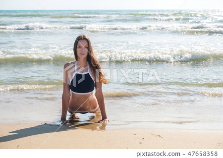 Young woman in bikini does Bhujangasana yoga asana or Cobra Pose on the sunny beach, front view. 47658358