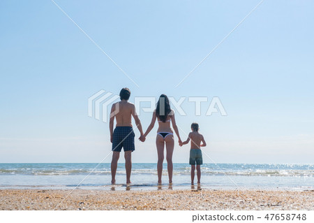 Unrecognizable family standing on the beach and looking at sea Mom son and dad hold hands back view. 47658748