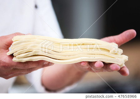 Pastry chef showing dough sheets ready to be rolled to produce croissant. 47658966