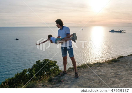 Son on the dad's hands on a mountain with seaside. Playing together at sunset. Fun pastime. Son on the dad's hands on a mountain with seaside. Playing together at sunset. Fun pastime. 47659187