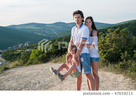 Family photo in the mountains mom, dad and son wearing light clothing. Son hanging in dad's hands. 47659213