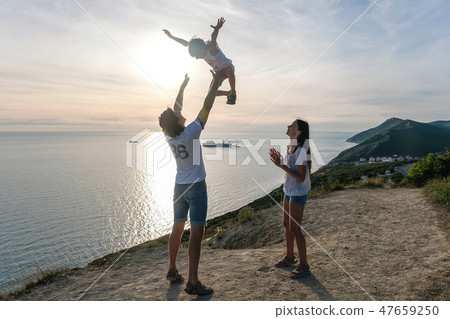 Dad throws his son in the air, and mom looks at them on the mountain with seascape. Dad throws his son in the air, and mom looks at them on the mountain with seascape. 47659250