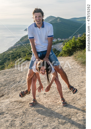 Woman lifts man. Fun pastime on the mountain with seascape. Vertical photo. Woman lifts man. Fun pastime on the mountain with seascape. Vertical photo. 47659262
