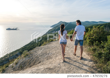 Couple man and woman walking on a country road in the mountains holding hands. back view. Couple man and woman walking on a country road in the mountains holding hands. back view. 47659278