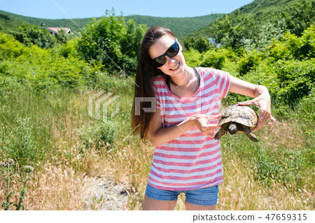 Woman brunette in sunglasses and striped t-shirt keeping turtle in her hands in the forest. Woman brunette in sunglasses and striped t-shirt keeping turtle in her hands in the forest. 47659315