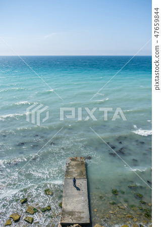Boy of 6y in jacket and jeans is standing on pier at sea during a storm with waves, afar view. Clear Boy of 6y in jacket and jeans is standing on pier at sea during a storm with waves, afar view. Clear 47659844