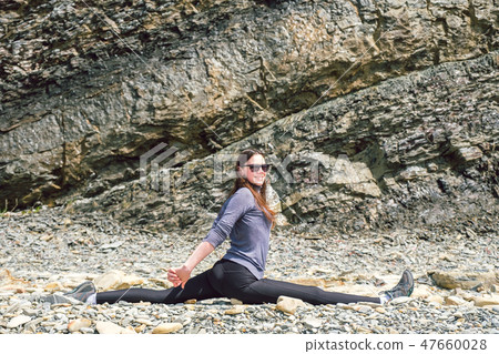 Side view of a healthy mature woman figure stretching and exercising on a rock platform 47660028