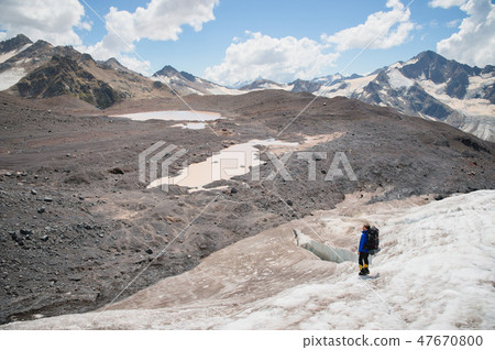 A mountaineer with a backpack walks in crampons walking along a dusty glacier with sidewalks in the A mountaineer with a backpack walks in crampons walking along a dusty glacier with sidewalks in the 47670800