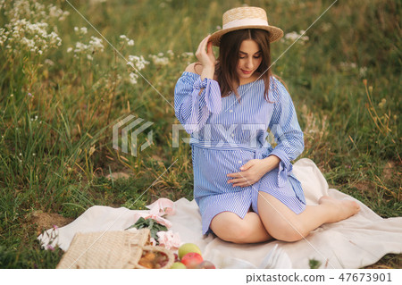 Young pregnant woman sitting in the field and relax. She took a fruit basket. Summer Young pregnant woman sitting in the field and relax. She took a fruit basket. Summer 47673901