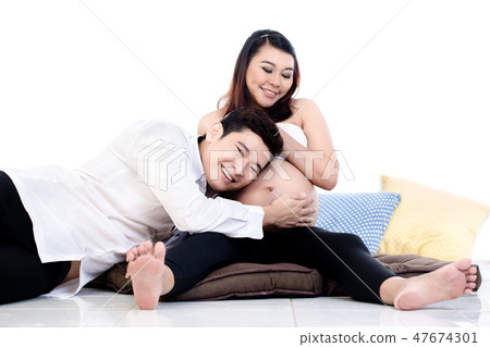 Man listening to his wife's belly sitting on floor 47674301
