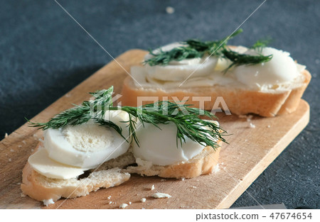 Closeup two sandwiches with bread, butter, eggs and dill on wooden board in black background. Making 47674654