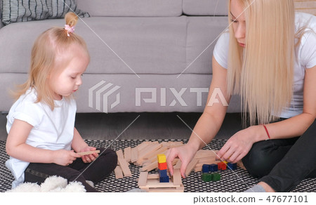 Mother and daughter build from wooden bricks sitting on the floor by the couch. Mother and daughter build from wooden bricks sitting on the floor by the couch. 47677101