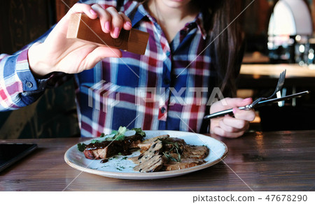 Closeup woman's hand pepper piece of pork cooked on the coals with potatoes, gravy and greens on 47678290