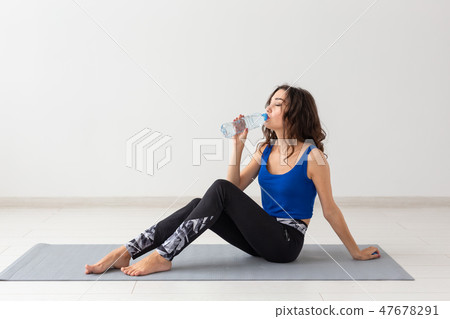 Healthy lifestyle, people and sport concept - Young beautiful woman practicing yoga and drinking 47678291