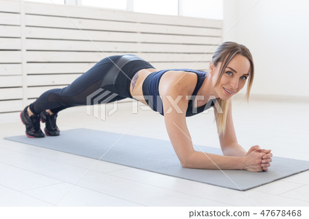 Sport, yoga and people concept - a young woman is doing a plank, taking a balance Sport, yoga and people concept - a young woman is doing a plank, taking a balance 47678468