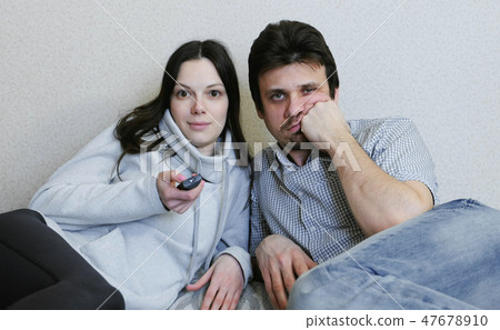 Couple watching TV lying on the couch. Woman switches channels and watching with interest and man is 47678910
