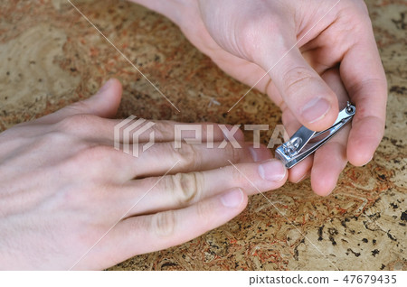 Man is cutting his nails by Clippers on the table. Close-up fingers. Wood backgound. Man is cutting his nails by Clippers on the table. Close-up fingers. Wood backgound. 47679435