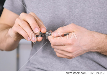Man is cutting his nails by Clippers. Close-up hands.Grey t-shirt in the background. Man is cutting his nails by Clippers. Close-up hands.Grey t-shirt in the background. 47679442
