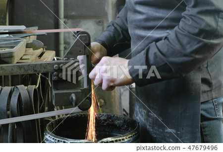 Grinding billets of metal on a belt-grinding machine. Close-up of a man's hand. 47679496