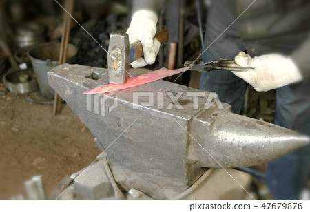 Making the knife out of metal at the forge. Close up blacksmith's hands hitting hot metal with a 47679876