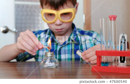 Experiments on chemistry at home. Boy sets the burning alcohol lamp on fire with a match. Experiments on chemistry at home. Boy sets the burning alcohol lamp on fire with a match. 47680540