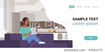 woman listening audio book through headphones african american girl using tablet sitting on couch 47682573