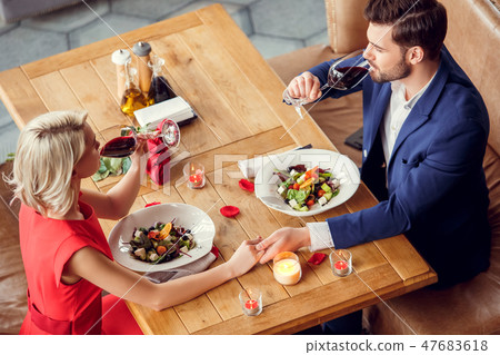 Young couple on date in restaurant sitting eating salad drinking wine holding hands top view 47683618