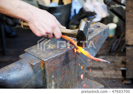 Blacksmith working metal with hammer on the anvil 47683700