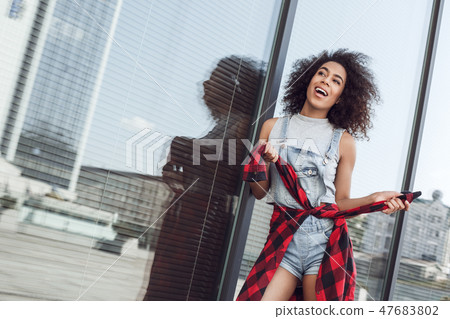 Young woman in the city street near window holding jacket sleeves looking aside excited 47683802