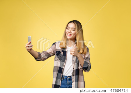 Pretty girl take a self portrait with her smart phone. Asian girl selfie, isolated on yellow Pretty girl take a self portrait with her smart phone. Asian girl selfie, isolated on yellow 47684714