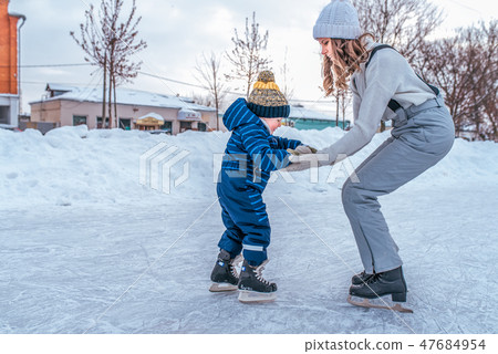 A young mother holds the hand of a little boy 2-4 years old child. In winter, on rink in city. Happy A young mother holds the hand of a little boy 2-4 years old child. In winter, on rink in city. Happy 47684954
