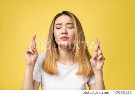 Young happy asian woman with fingers crossed on yellow background 47685125