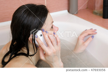 Young woman btunette taking on her mobile phone laying in the bathroom. 47693056